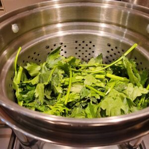 Steamed greens in a metal colander.