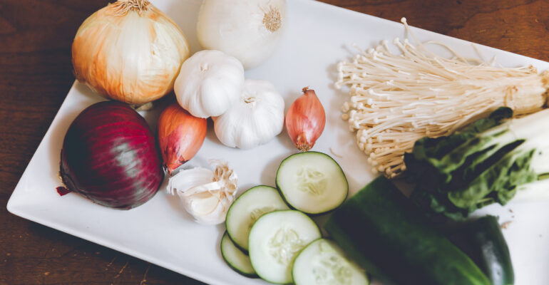 Fresh vegetables including onions, garlic, and cucumbers on a white plate.