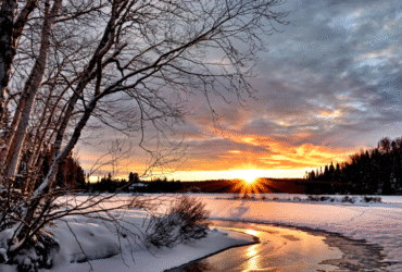 Winter sunset over snowy landscape and river.